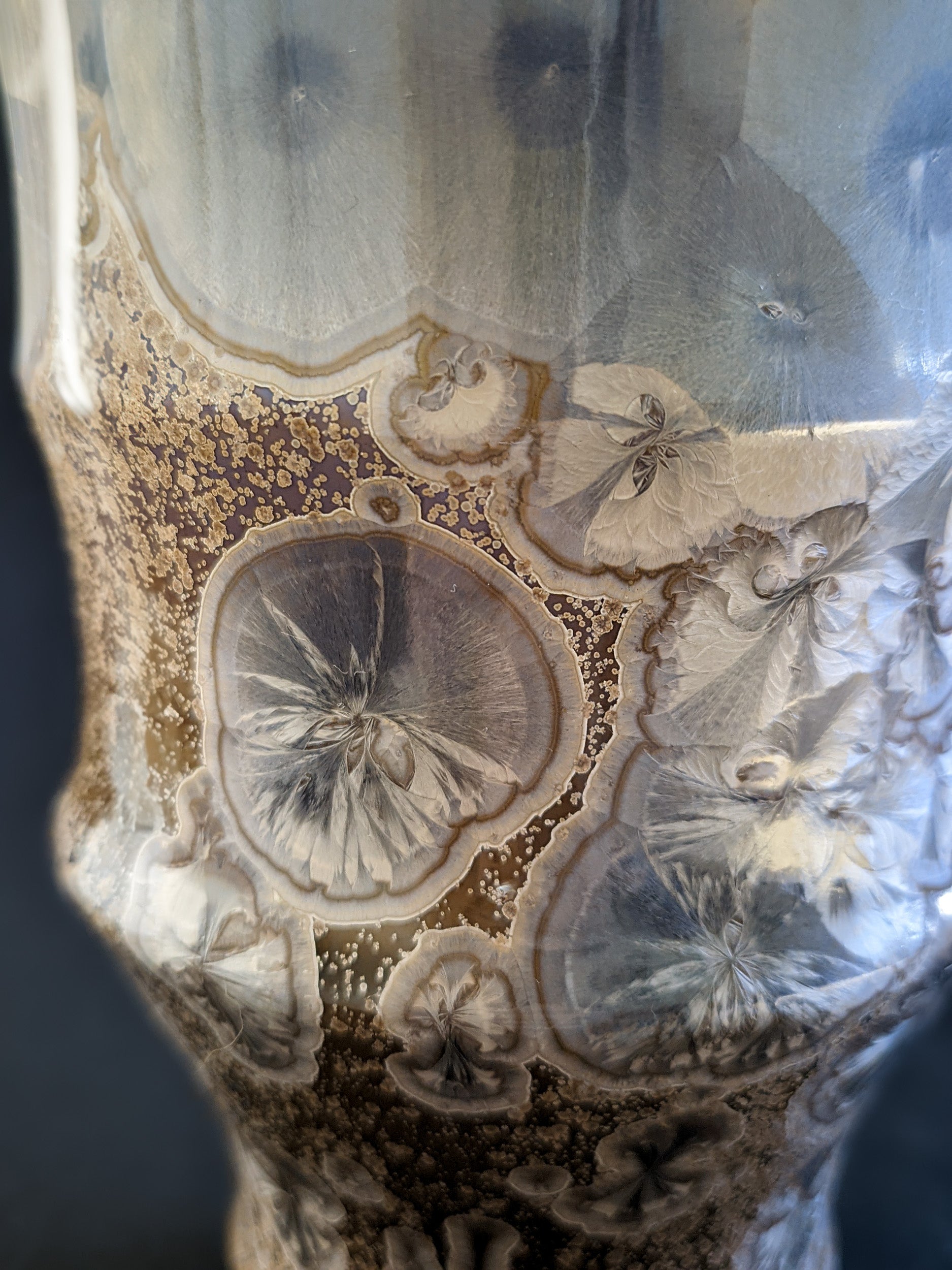 A detailed view of a large, metallic blue crystal in the center of the vase, surrounded by the warm amber glaze, highlighting the intricate crystalline patterns.