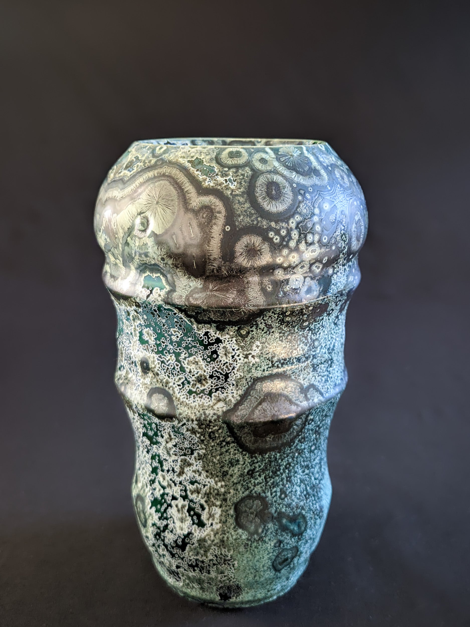 Emerald green crystalline-glazed vase with large nickel and gold-toned crystals, each framed by white rings. 