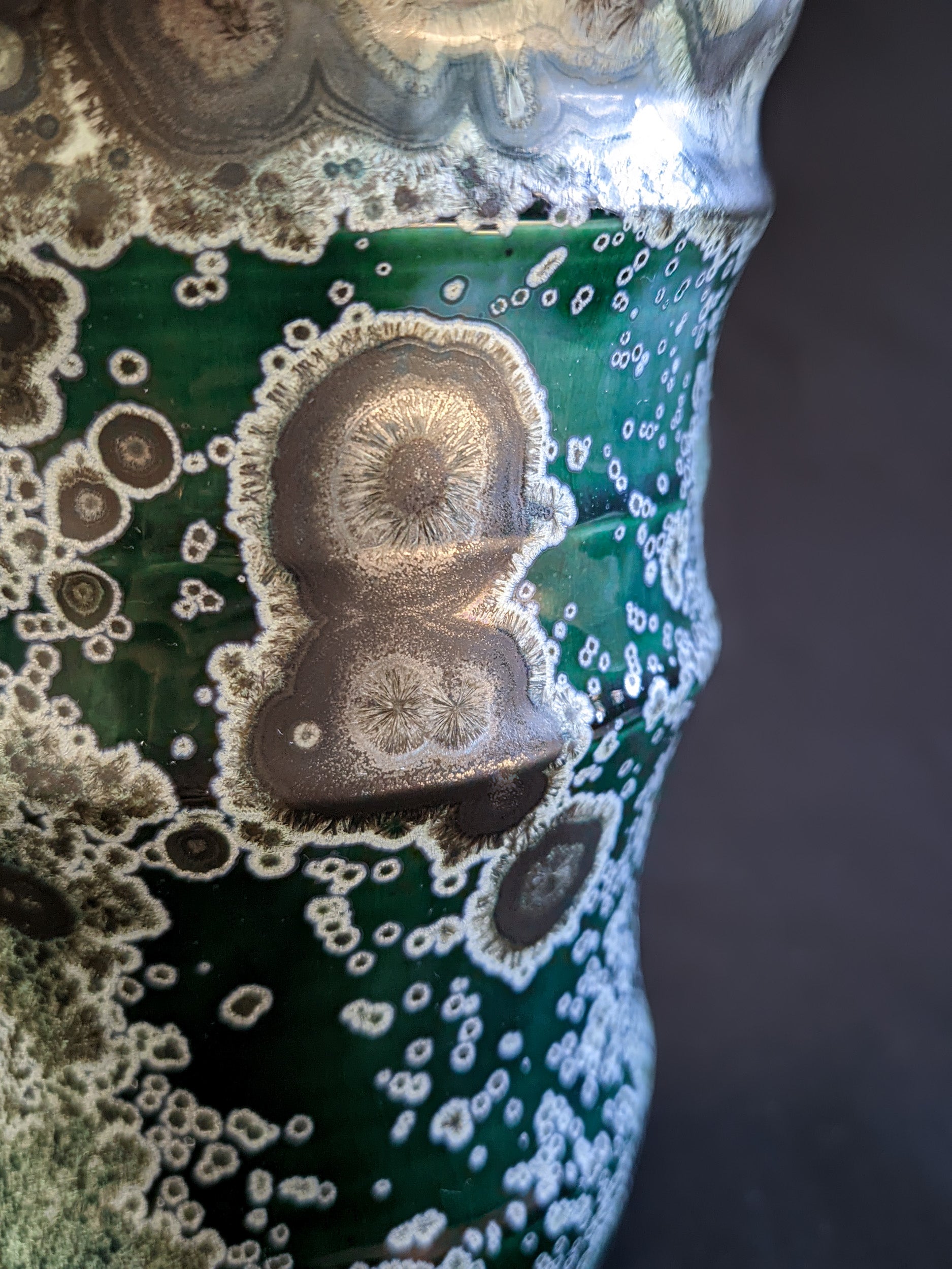 Macro shot of crystalline glaze featuring large gold and nickel-hued formations with delicate white rings and dense secondary white crystals.