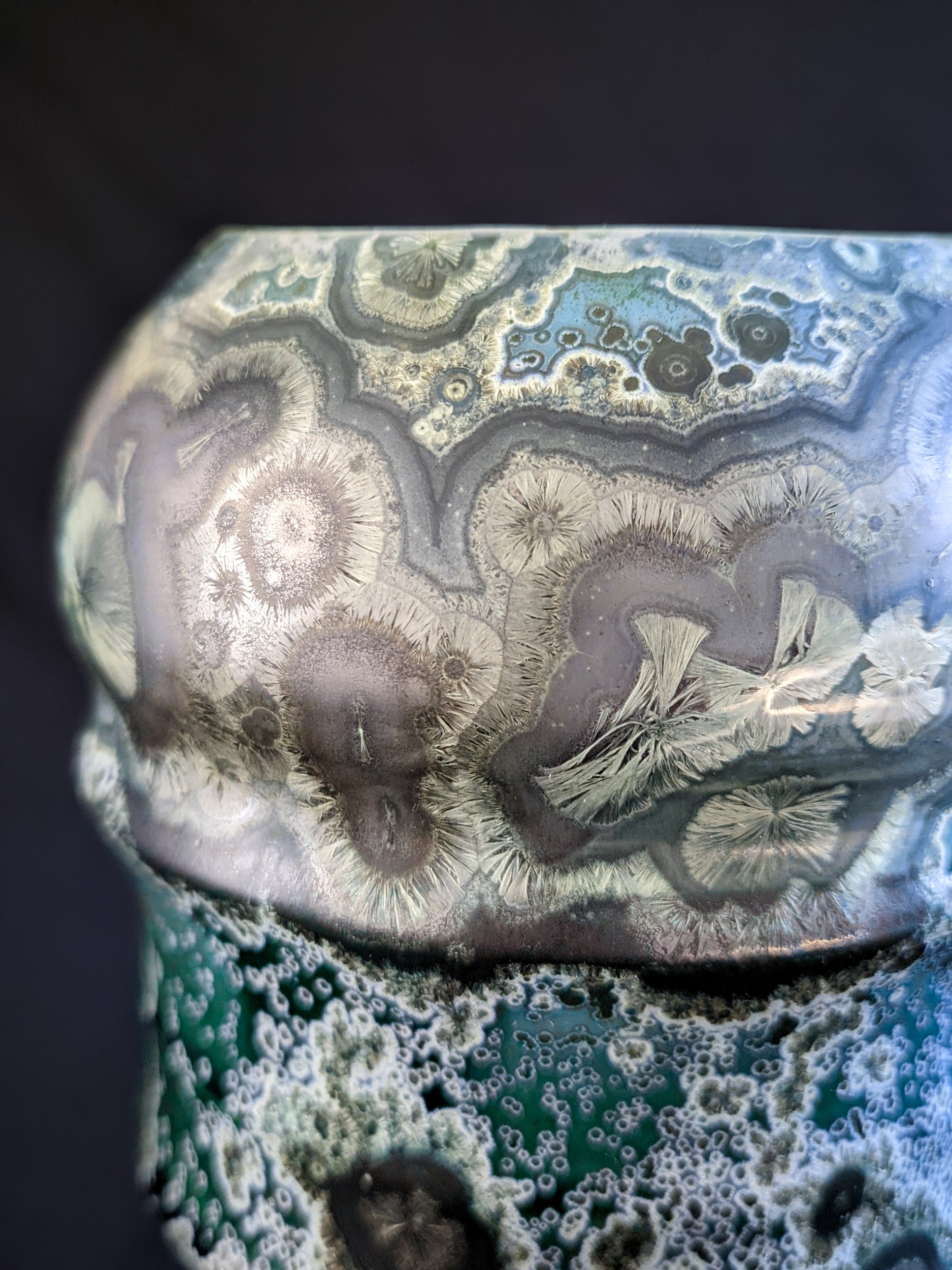 Detail shot of crystalline glaze featuring large gold and nickel-hued formations on an emerald green background.