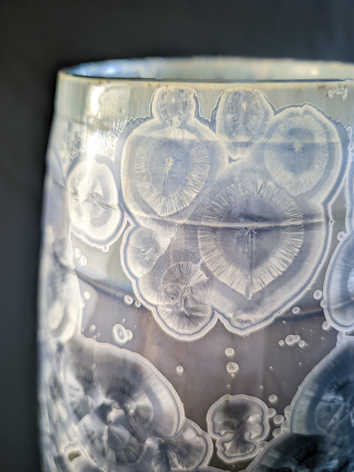 Close up of large, sculptural vase with a wide opening, showcasing a dramatic color gradient from dark blue to light purple and white. The vase is adorned with overcrystallized blue crystals with white rings, creating an artistic texture.