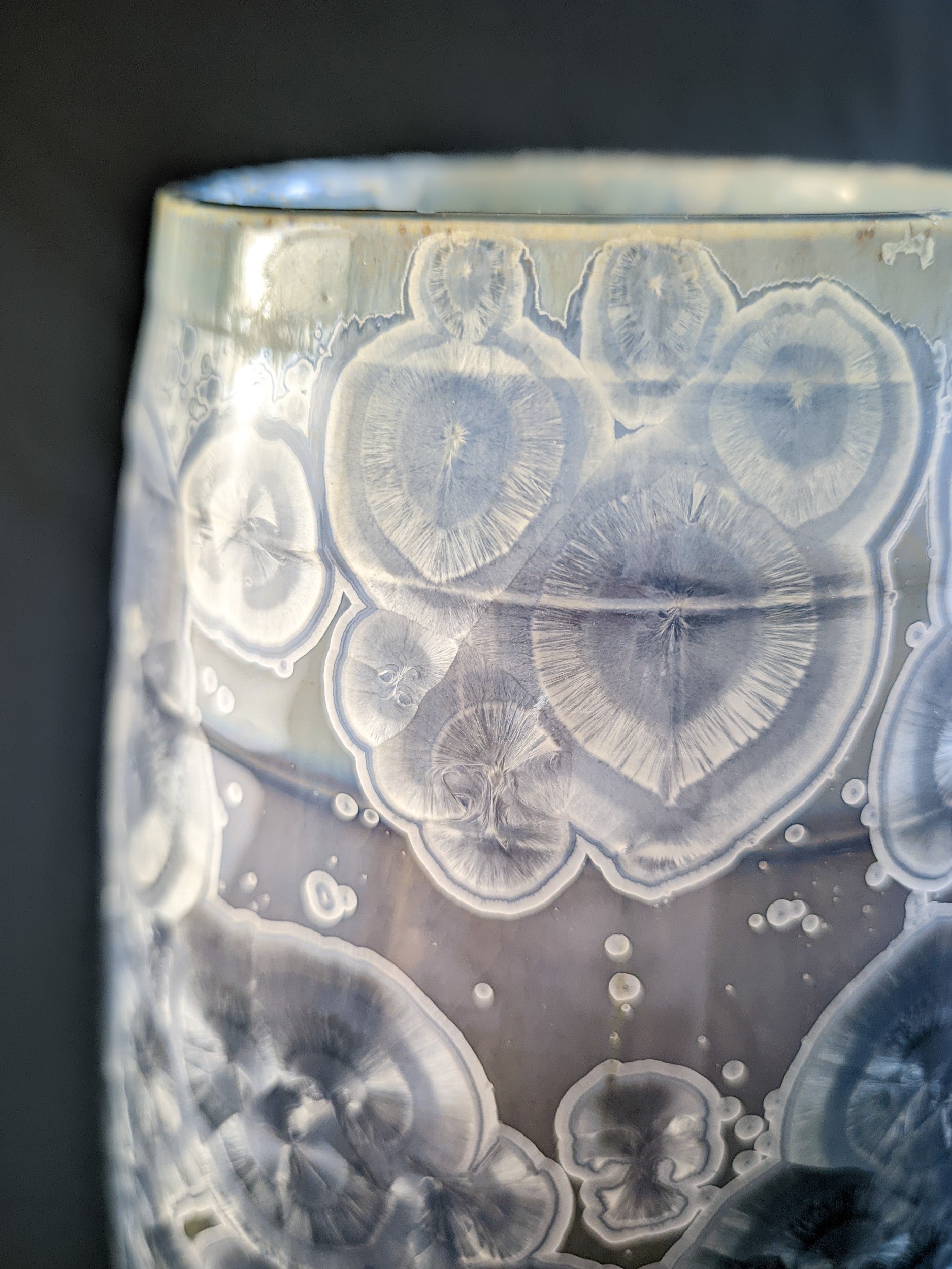 Close up of large, sculptural vase with a wide opening, showcasing a dramatic color gradient from dark blue to light purple and white. The vase is adorned with overcrystallized blue crystals with white rings, creating an artistic texture.