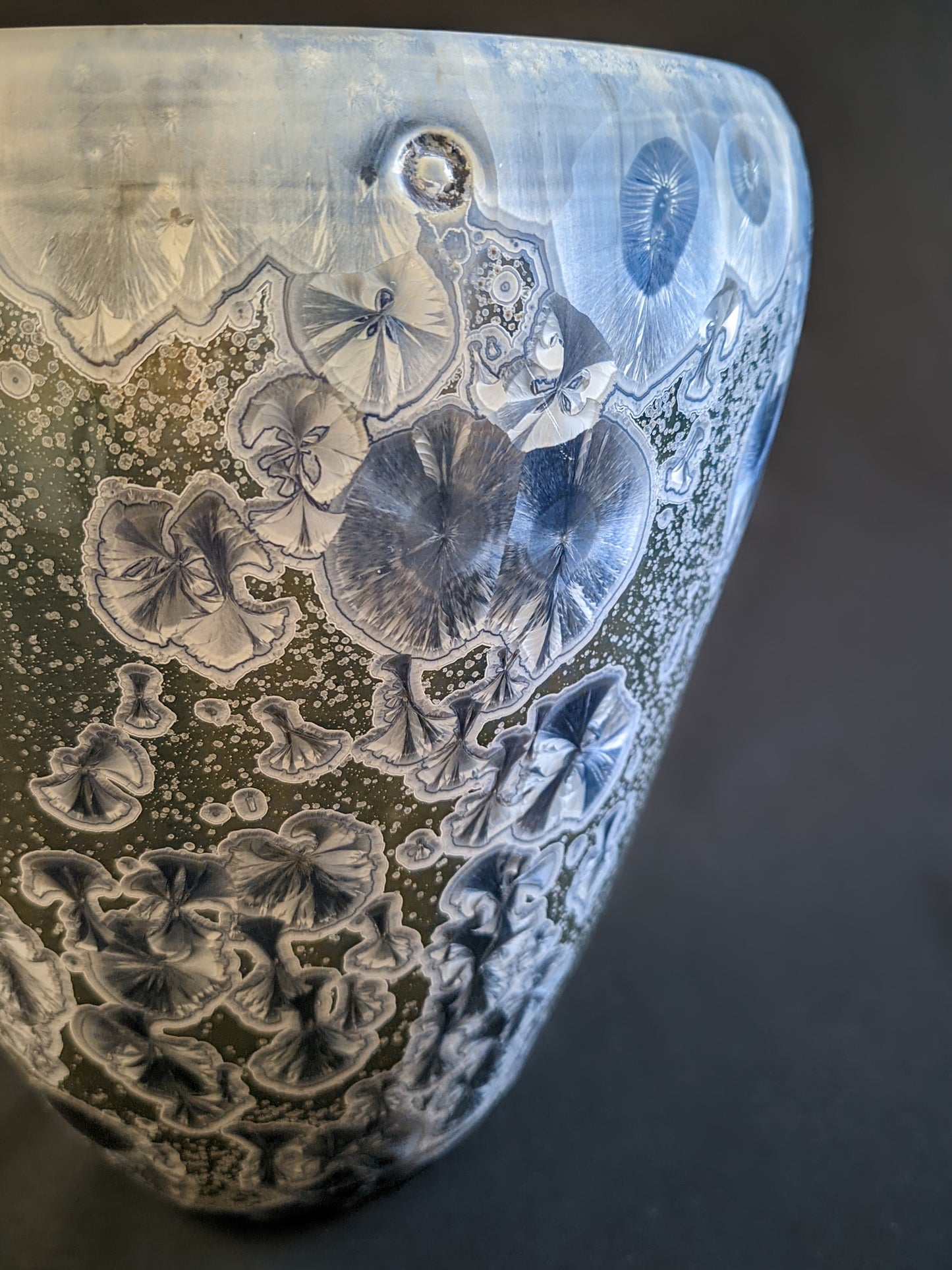 A detailed close-up of deep blue and light blue crystals with delicate white rings on a muted green background, dusted with tiny secondary white crystals.